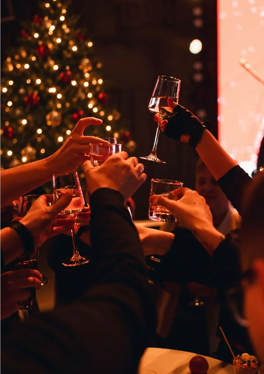 Guests raising their glasses in a toast in front of a lit Christmas tree